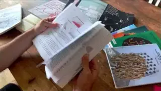 A researcher looking through various books and papers on a table.