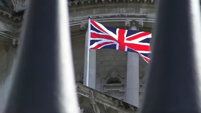 A Union Jack flag flies on a building, representing the UK government.