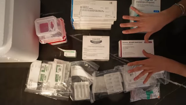 Various medications, syringes, and a sharps container laid out on a table, illustrating the supplies needed for hormone injections