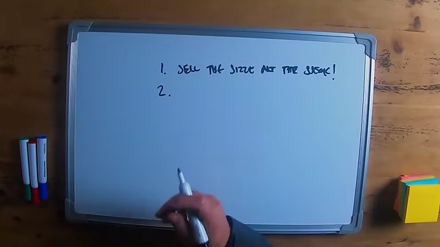 The speaker writing "sell the sizzle not the steak!" on a whiteboard as a sales principle.