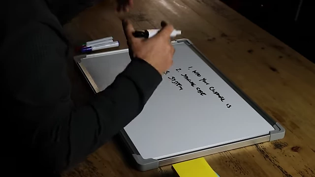 The speaker writing "systems" on a whiteboard as the third point for marketing.