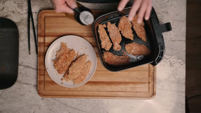 Spritzing olive oil onto the coated chicken tenders in the air fryer