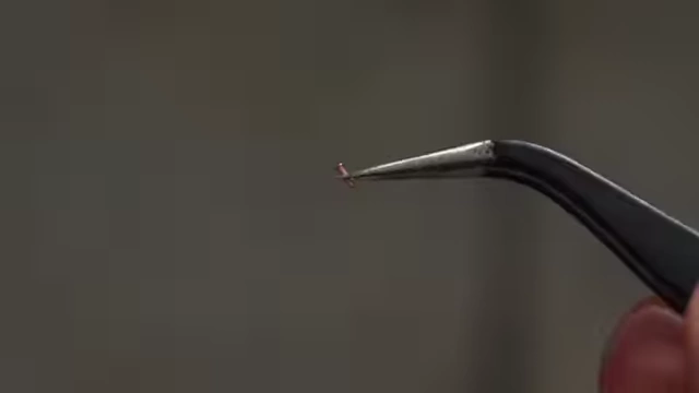 A small rivet held by tweezers, illustrating the manual installation required for traditional vias