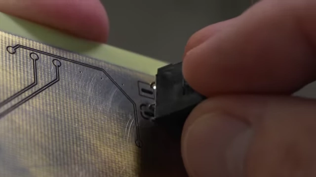 A through-hole barrel jack being inserted into a laser-drilled hole on the PCB