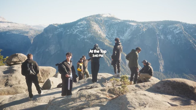 A group of hikers standing on a rocky outcrop, overlooking a vast valley, with "At the Top 3:40 PM"