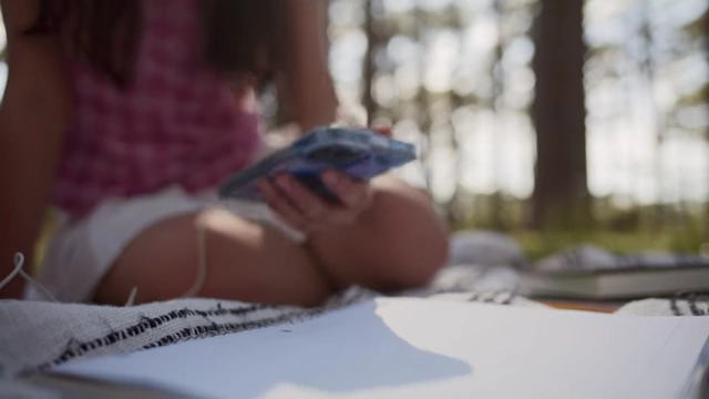 A person sitting outdoors, drawing in a sketchbook