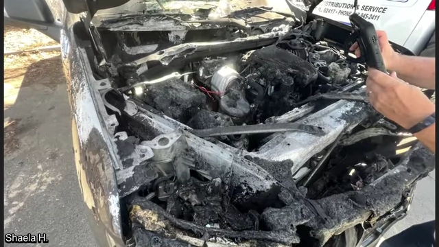 A severely burned truck, showing extensive fire damage to the engine bay and front end.