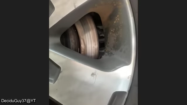 A view of a vehicle's rear wheel, showing severely corroded and damaged brake components.
