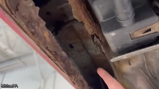 A large hole in a rusted pinch weld on a vehicle.