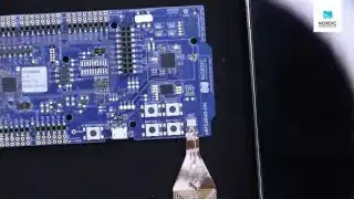 An nRF52840 Development Kit connected via USB, alongside a smartphone, ready for Bluetooth LE application development.