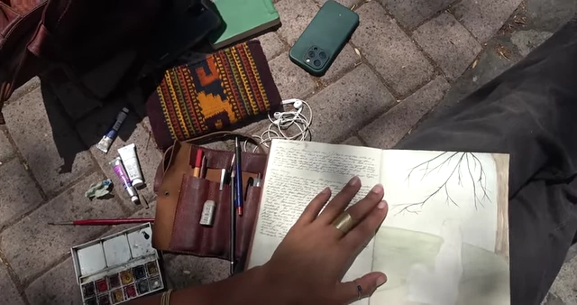 An open journal showing both writing and a nature sketch, surrounded by art supplies.
