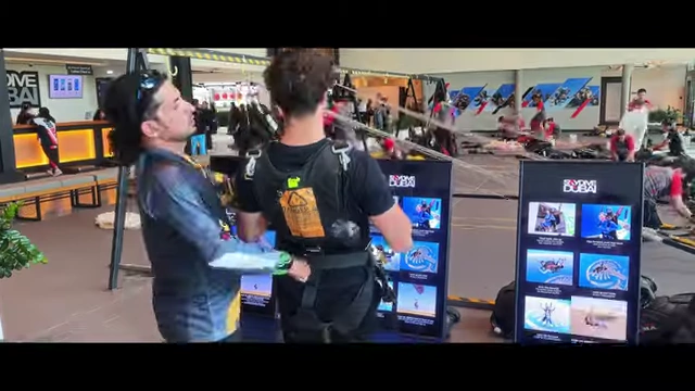 Alex Shane preparing for a skydive, wearing a harness and interacting with instructors, emphasizing the physical preparation for high-stakes activities
