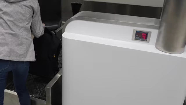 A person weighing luggage at an airport check-in counter, displaying a digital weight reading.