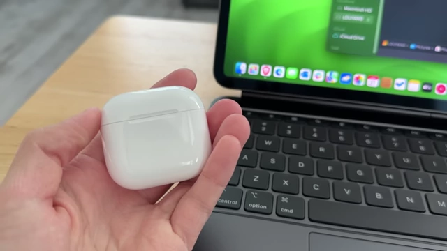 A pair of white Apple AirPods in their charging case, held in a hand.