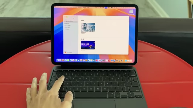 A hand typing on the Magic Keyboard while the iPad Pro displays the macOS Music app via Sidecar.