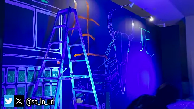 An artist working on a mural with glow-in-the-dark paint in the Low Light Area.