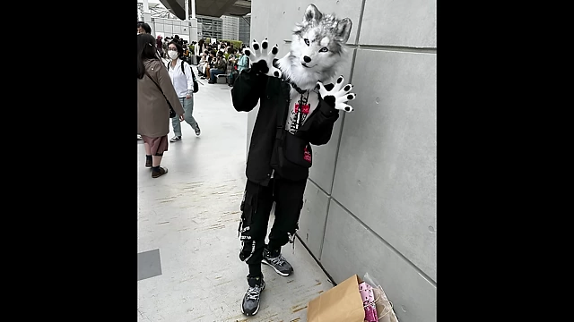 A fursuiter in a grey wolf head and streetwear outfit, posing for a photo.