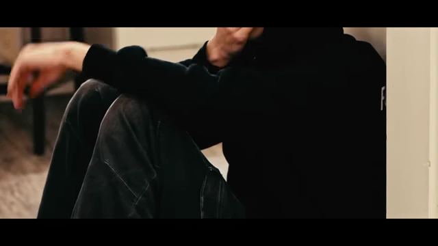 A person in a black hoodie is slumped against a wall in a kitchen, appearing distressed and symbolizing McSwee at his lowest point.