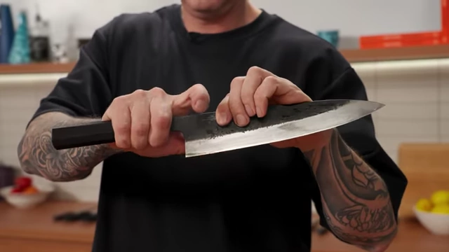 A chef demonstrates the correct grip for a chef's knife, with thumb and index finger on the blade