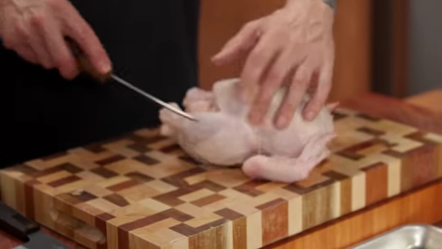 The chef cuts the chicken leg by inserting the boning knife between the drumstick and breast