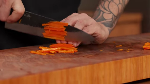 A chef juliennes carrots by stacking thin planks and slicing them into matchsticks