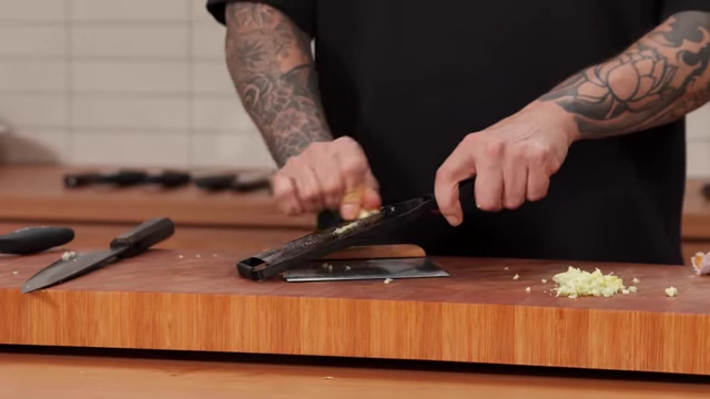 A chef grating garlic using a microplane over a bench scraper, preventing contact with the cutting board