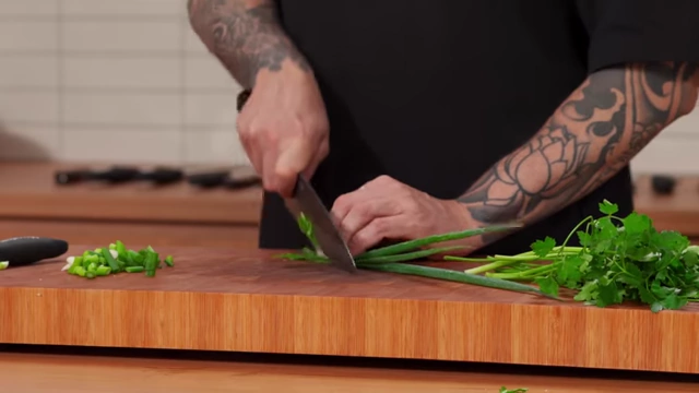 A close-up of a chef finely slicing the green parts of spring onions at an angle, held together tightly