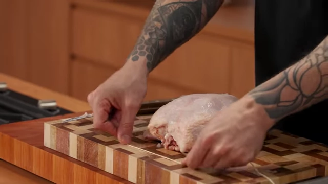 A chef positions butcher's string under the wings of a raw chicken for trussing