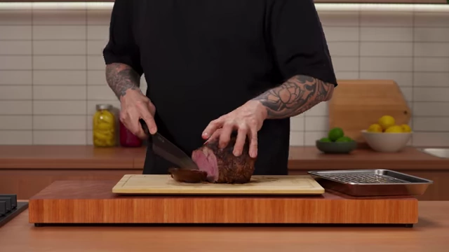 A chef slices a perfectly rested roast beef against the grain, revealing the internal cooked temperature