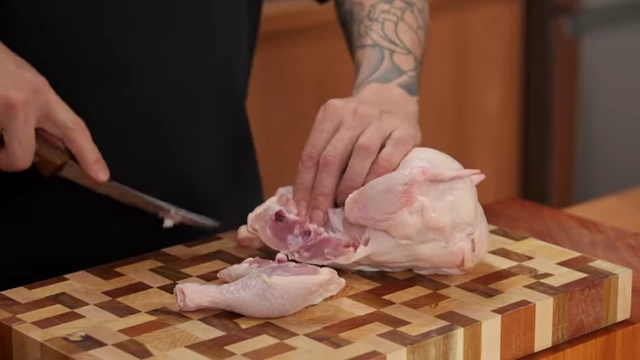 A boning knife separating a raw chicken leg from the carcass