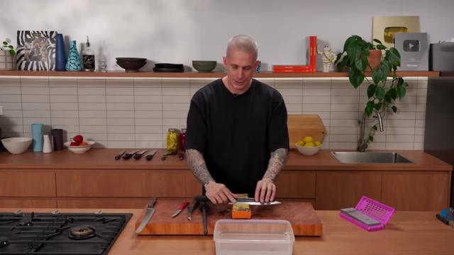 A chef pulls a knife blade towards himself along a wet stone to remove the burr