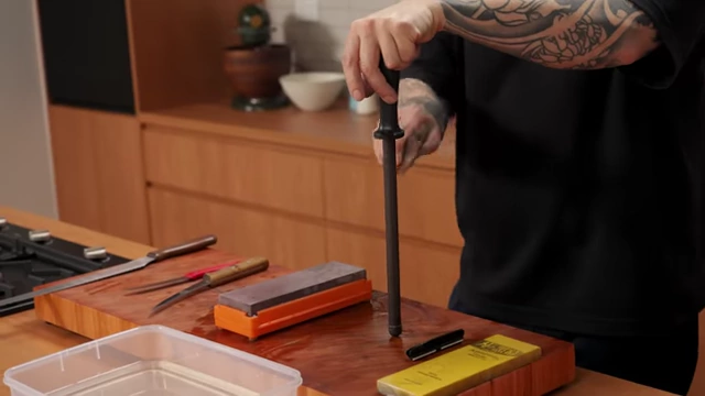 A chef hones a knife on a vertical honing rod on a cutting board