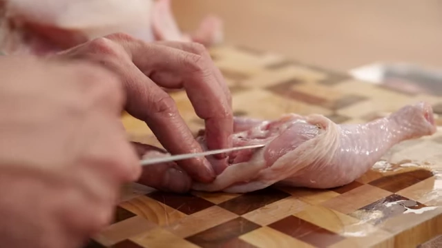 A chef locates the joint between the drumstick and thigh with a finger before cutting