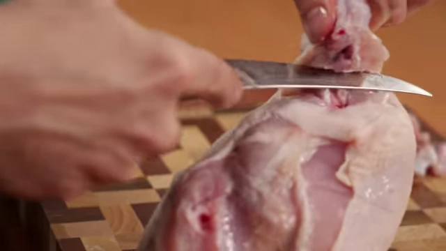A chef cuts through the joint to remove the chicken wing from the carcass