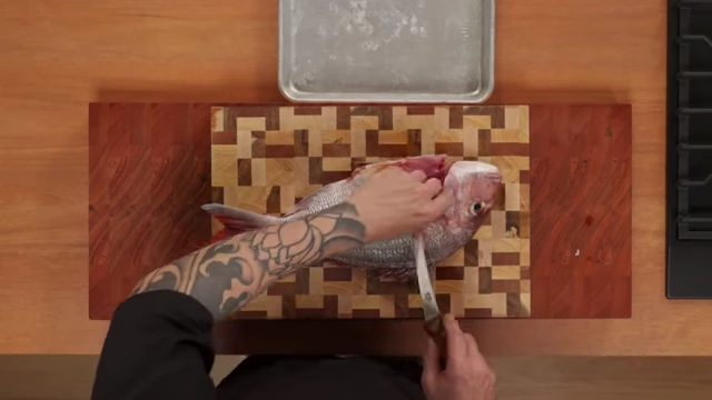 An overhead view of the chef making an incision behind the fish's head, along the spine