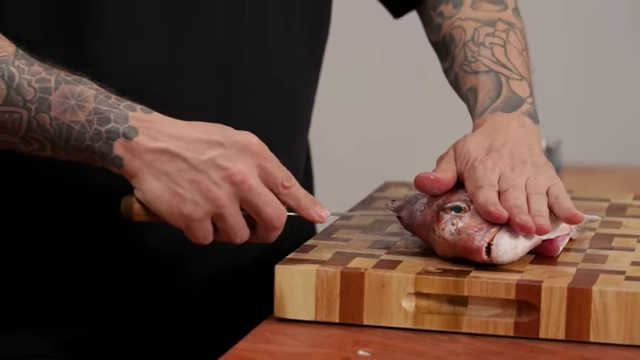 A chef carefully runs a boning knife along the fish's spine to separate the fillet