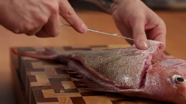 A chef carefully separates the belly section of the fish fillet from the frame
