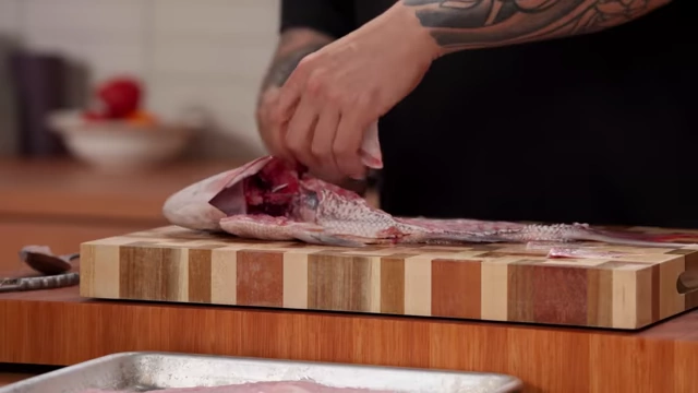 A chef separates the collar from the fish carcass, preparing it for grilling or stock