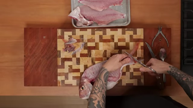 A chef uses kitchen shears to segment the fish carcass for fish stock
