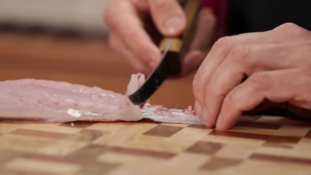 A chef demonstrates the correct angle of the knife to separate skin from fish fillet
