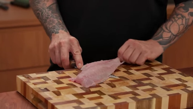 A chef wiggles the skin back and forth to separate it from the fish fillet, leaving the blade stationary