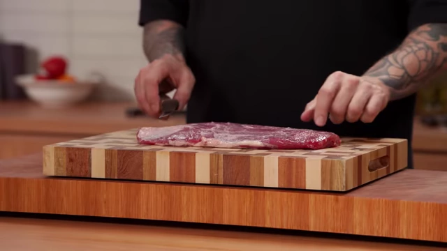 A raw flank steak lies on a cutting board, with silver skin visible on its surface