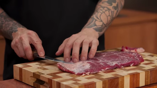 A chef skillfully removes silver skin from a flank steak using the tip of a boning knife