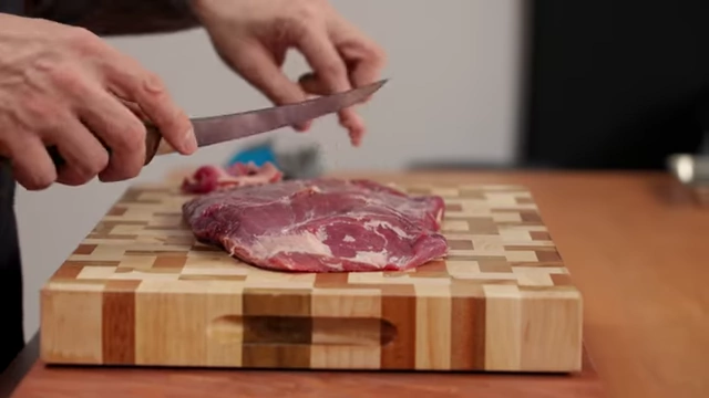 A chef removes translucent membrane from a piece of beef with a boning knife