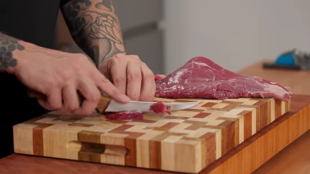 A chef slices raw beef into small, even pieces for stir-frying