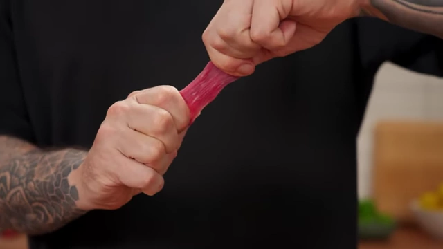 Hands struggling to pull apart a piece of beef cut with the grain, demonstrating its toughness