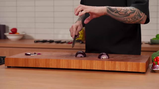 A chef demonstrates the "claw" grip, where fingers are curled to protect them while slicing an onion