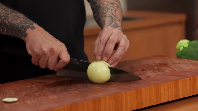A chef makes horizontal slices into half an onion, keeping the slices connected at the root