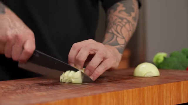 A chef turns the onion half and makes vertical cuts to create a large dice
