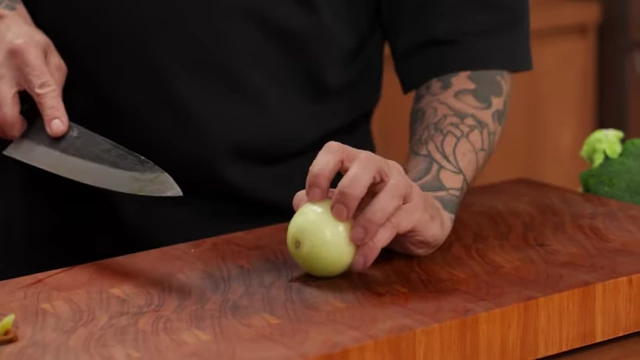 A chef stabilizes a whole onion with his palm while slicing it into rings